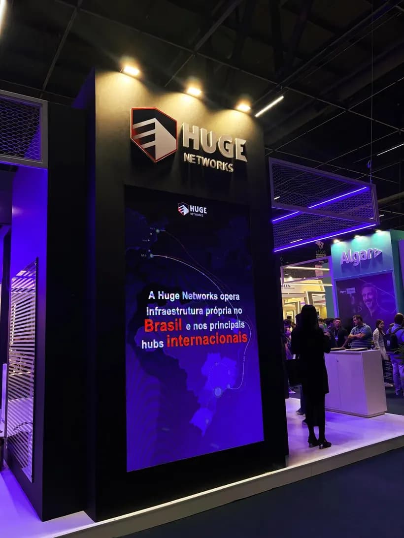 Painel do estande da Huge Networks destacando infraestrutura própria no Brasil e em hubs internacionais